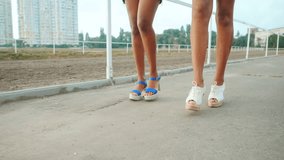 Legs of beautiful afro-american women friends walking outdoor. Young mixed race girls wearing heels, colorful clothing communicates, enjoys the meeting in slow motion. Dolly shot.