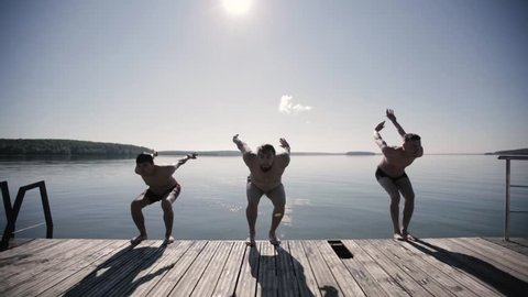 Three guys do a somersault with their backs forward jumping into the water