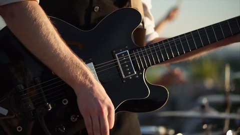 close up shot of the rhythm of the guitar, the men's hands touch the strings and get an energetic melody outdoors during the day, the person holding the mediator