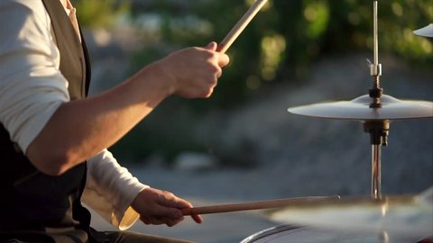 close up shot of the men's hands, who holds the drumsticks in their hand, the people energetically hit them on the plates in the daytime outside, maybe this is a street musician