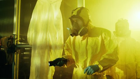 Two Officers from Hazardous Materials Police Unit Inspect Busted Drug Making Laboratory. They Wear Hazmat Suits and Gas Masks and Walk Carefully with Flashlights. Shot on RED EPIC-W 8K Helium Camera.