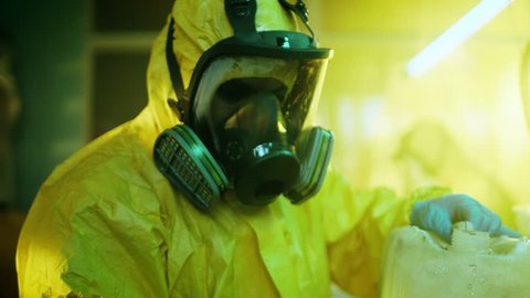 In the Underground Drug Laboratory Clandestine Chemist Wearing Protective Mask and Coverall Mixes Chemicals. He Pours Liquid From Canister into Bowl, Toxic Compounds Create Smoke. 4K UHD.