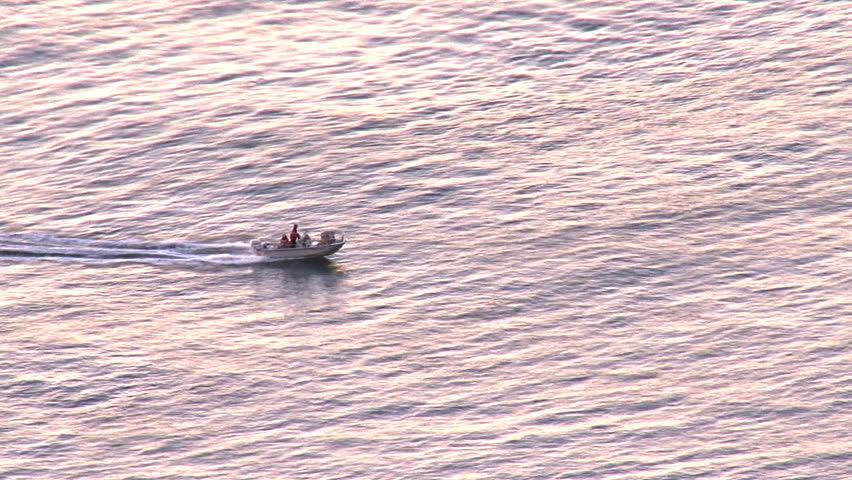 Open-hulled boat being piloted at high speed across bay waters which glow