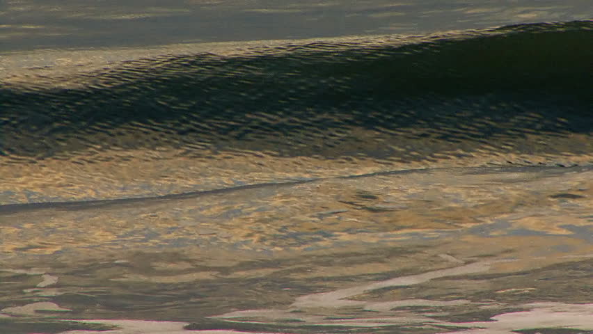 Close tele shot of waves as they approach the shore from the bay in evening. The