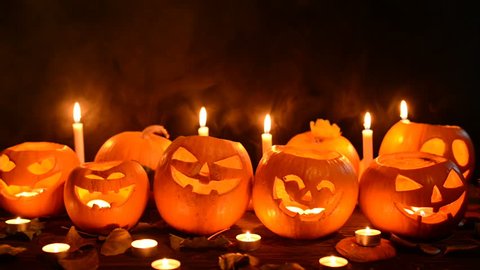 Halloween pumpkins with candles over dark background, closeup, front view, locked down video