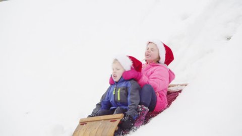 Brother and sister riding on a sled, winter day.