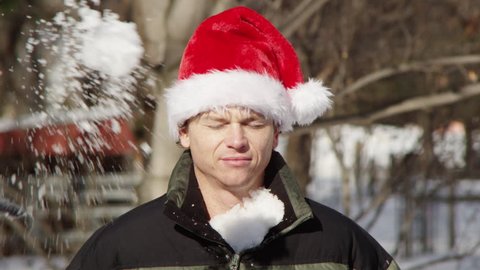 Man weating Santa hat, hit in the face with a snowball.