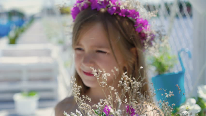 Portrait of cute little girl with wildflowers in the hands looking at camera 4K