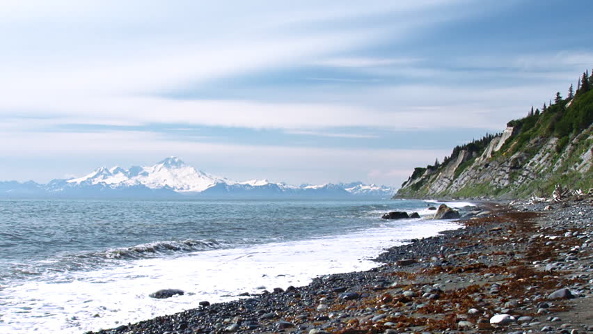 The waters of the Cook Inlet lap ceaselessly at a gravel and sand beach, the