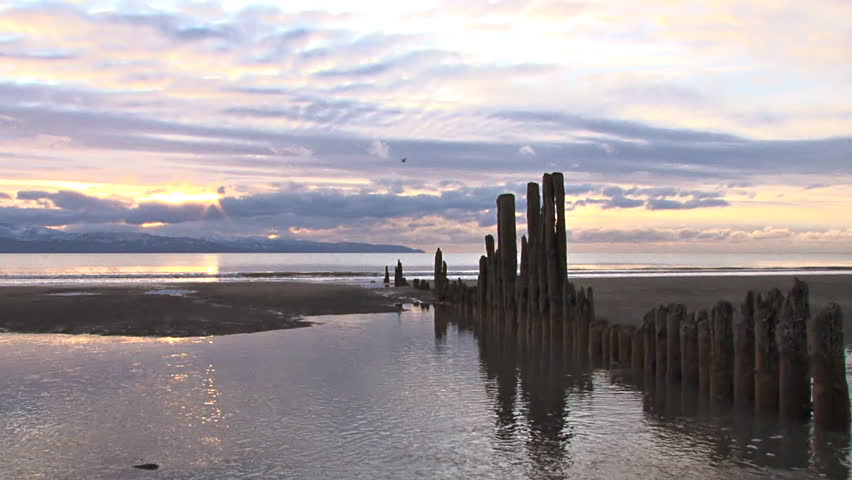 The sun sets on a rare calm day at low tide over Kachemak Bay. The pilings are
