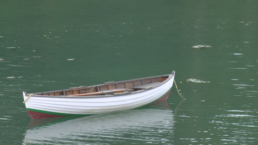 Double-ended rowboat floating at its mooring in green water.