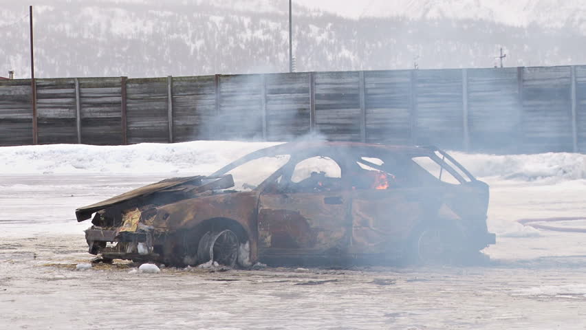 Derelict car burns alone in an icy lot.