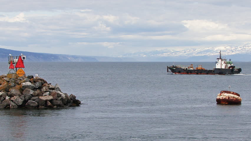 Large industrial landing craft leaving Homer Harbor, moving past the breakwater
