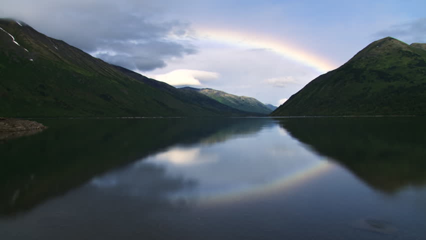 A very long-lasting rainbow moves down valley (and reflected in lake) as a storm