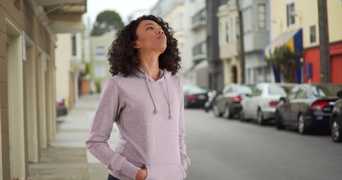 Portrait of attractive black female taking a breath outside on street, closing eyes in bliss. Pretty African American woman with curly hair titling face up towards sky, smiling peacefully. 4k