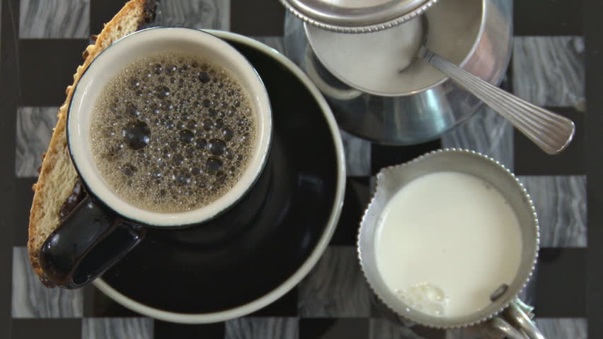 Pouring cream into a cup of coffee, then adding sugar and stirring. Situated on