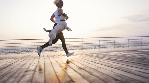 Young woman running with cute dog Jack Russel near the sea, slow motion