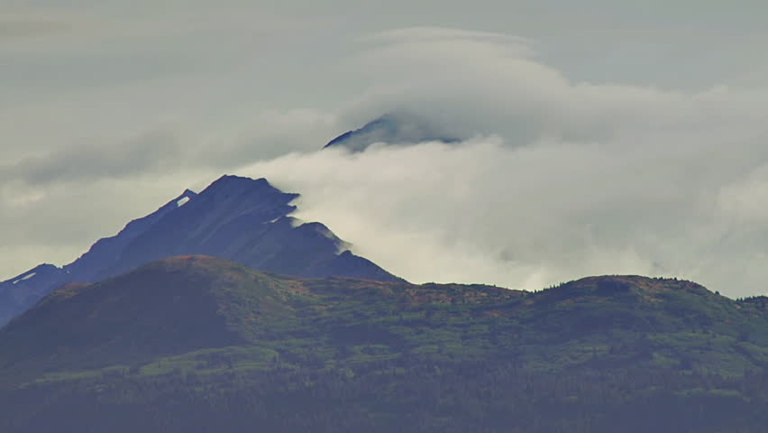 Vigorous winds distend thick clouds attached to a mountain ridge.
