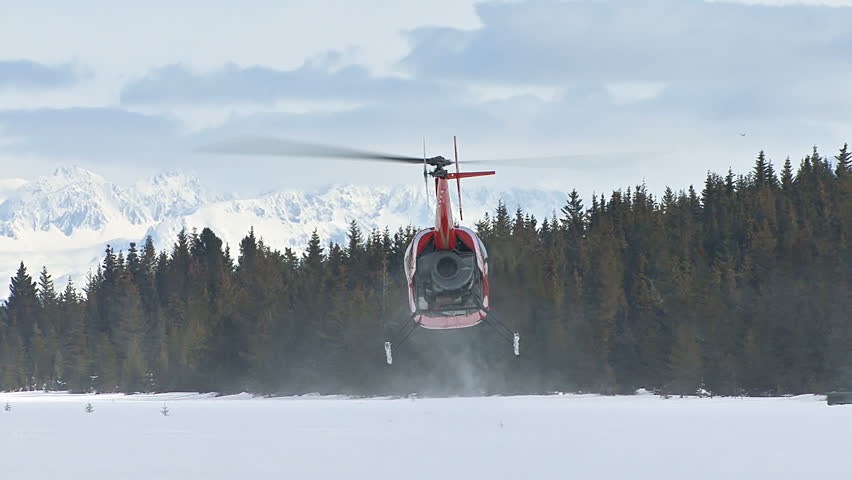 Red 2-man helicopter (Robinson R22) ascending and flying toward distant snowy