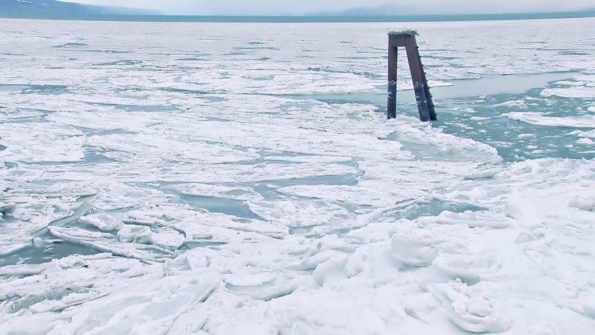 Relatively wide shot of broken sea ice moving around a mooring stanchion in
