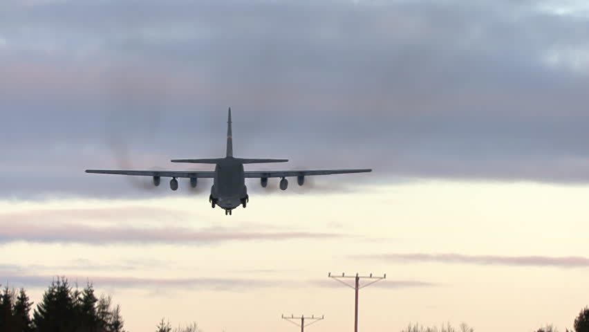 Air Force C130 landing over trees in evening.