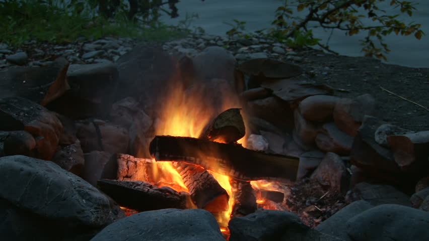 Classic campfire burning brightly with snapping flames by riverside at night.