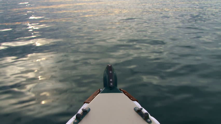 A sunset's light plays across smooth calm waters as seen from the bow of a small