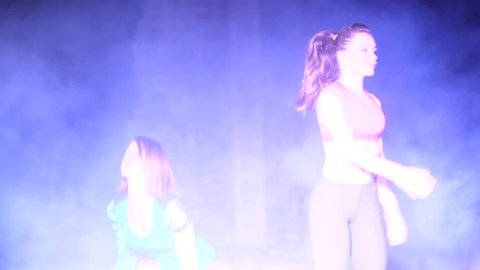 athletic sexy women, doing fitness exercises with weightings, At night, in light smoke, fog, in light of a stobascope and multicolored searchlights, in an old abandoned building