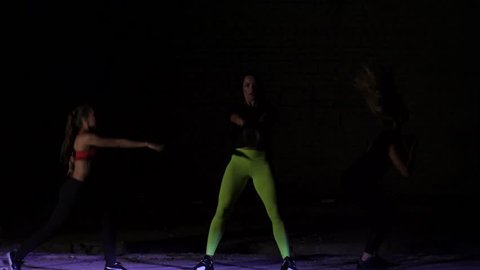 Four athletic sexy women, doing fitness exercises with weightings, At night, in light smoke, fog, in light of a stobascope, in an old abandoned hangar, building