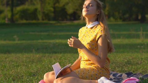 Slow motion. A young blonde girl in a warm sunny day at a picnic.green grass . holds in his hand a book and reads. rest in the park.