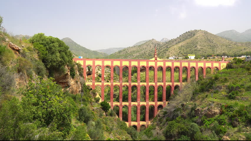 Huge pink and yellow the Aguadilla Aqueduct in Nerja Spain there are cars passing by as it is used as a bridge as well