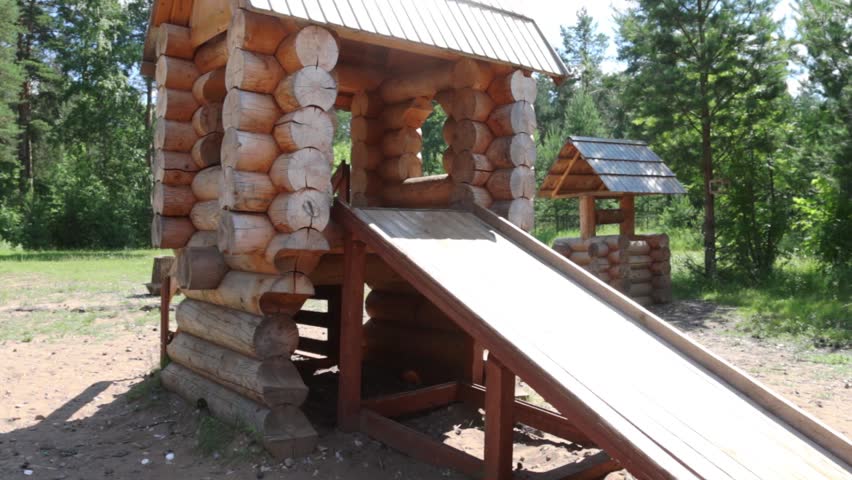 Happy little boy slides on wooden slide at playground at sunny day
