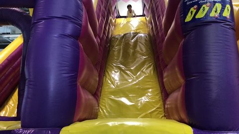 A Happy cute asian boy sitting on big inflatable slider toy and riding high in a slide.