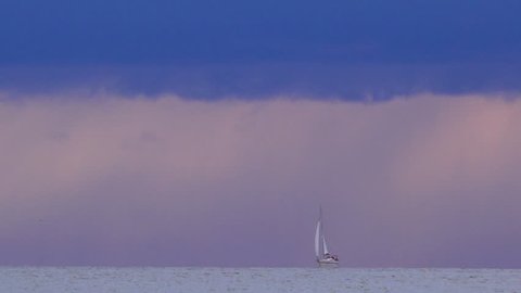 Sailing boat on the horizon changing direction just before the storm, dramatic rainy clouds in the background