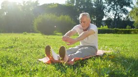 Pleasant aged man doing stretching exercises on the exercise mat
