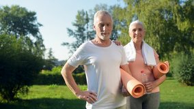 Cheerful senior couple standing in the park with the exercises mat