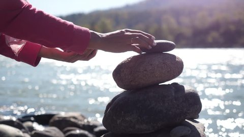 Female hands putting pebble stack next to the mountain river in slow motion. 3840x2160