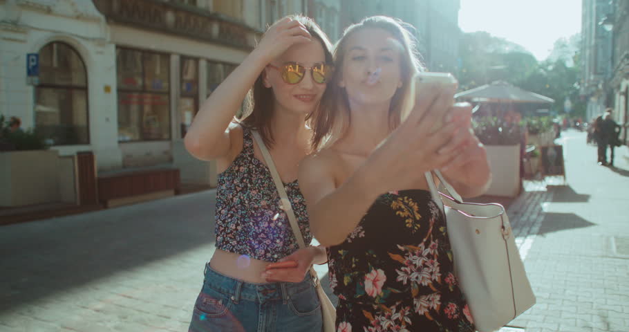 Two young beautiful girls taking selfie on a city street. 
