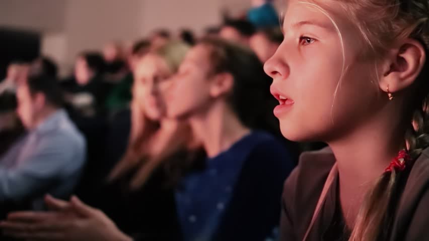 Teenage girl watches performance in theater, closeup