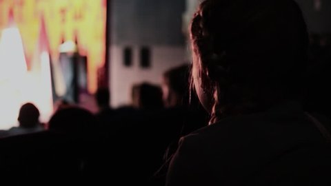 Girl watches performance in dark theater with bright stage, closeup