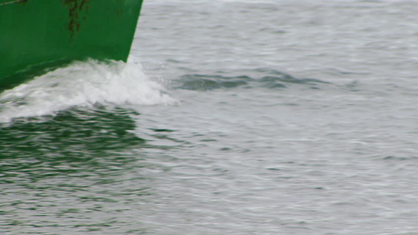 The battered, aged steel plate hull of a green boat splashes through small waves