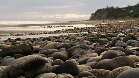 Long shot of a group of people relaxing at play on Bishop's Beach in Homer, AK, low angle with rocky beach exposed by low tide in foreground.