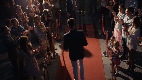Side-view scene, award ceremony concept, young man in business clothes walking across red carpet with photographers media press people applause fame fans grant prize triumph trophy handshaking reward