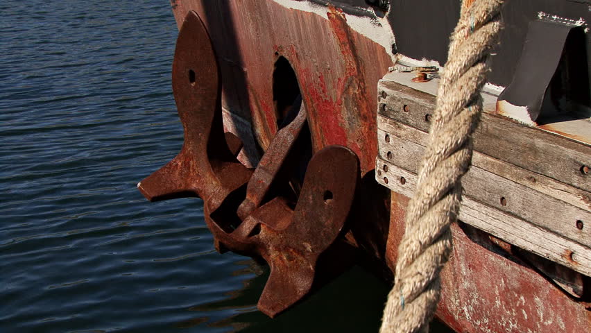 A large rusty anchor set against the bow of an old boat, reflections of the