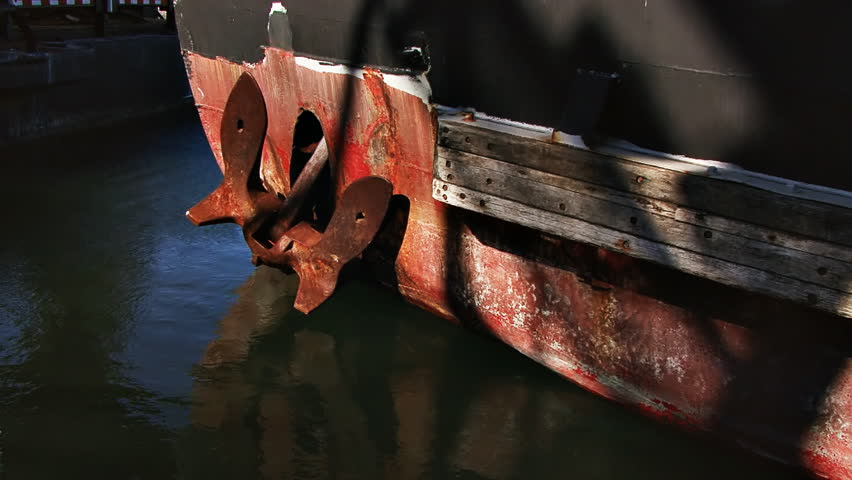 A large rusty anchor set against the bow of an old boat, reflections of the
