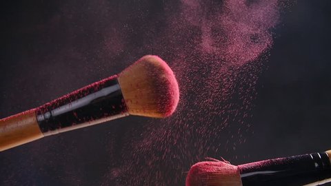 Two makeup brushes with powder on a dark background