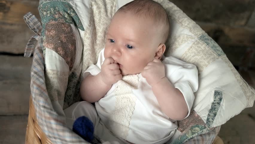 Baby with fingers in mouth. Infant child in a basket. The gift of new life.