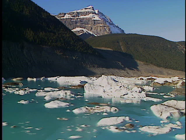Low level fly over alpine lake filled with melting icebergs from mountain