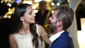 4k video honeymoon couple in evening outfit listening to music outdoors on terrace in greece village with lights in background
