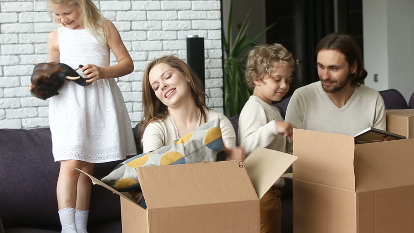 Happy excited family with two children unpacking boxes moving into new home concept, small kids helping parents with belongings in cardboards putting cushion on sofa in living room after relocation  Royalty-Free Stock Footage #31060987